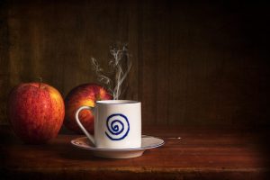 Steaming coffee cup beside fresh apples on a wooden table.