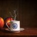 Steaming coffee cup beside fresh apples on a wooden table.