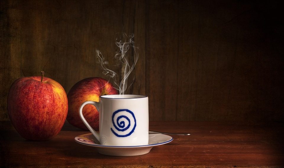 Steaming coffee cup beside fresh apples on a wooden table.