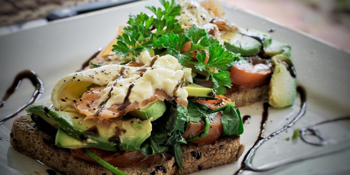 Open-faced toast with avocado, tomato, and poached egg drizzled with balsamic glaze.