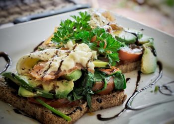 Open-faced toast with avocado, tomato, and poached egg drizzled with balsamic glaze.