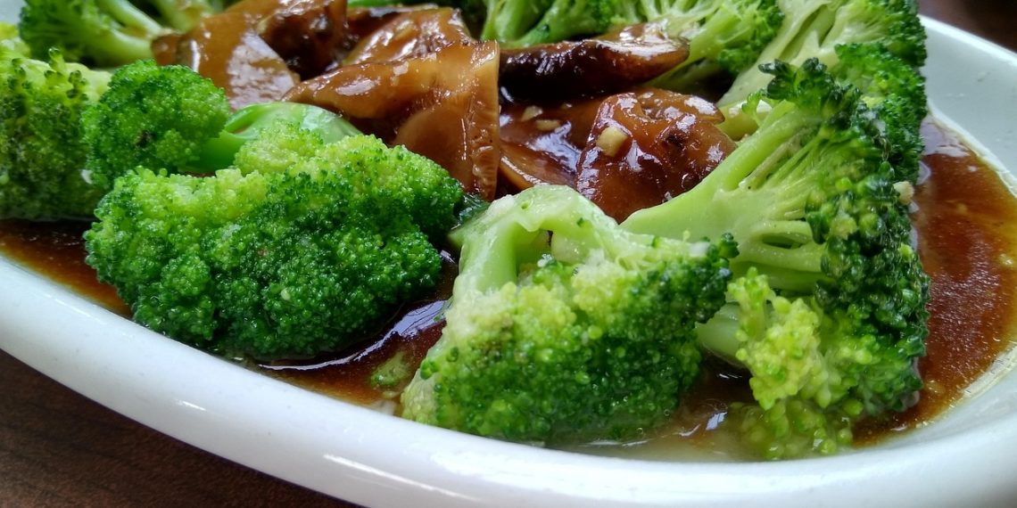 Steamed broccoli in savory sauce with mushrooms on a white plate.