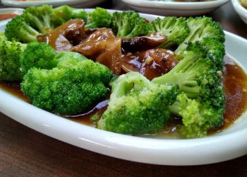 Steamed broccoli in savory sauce with mushrooms on a white plate.