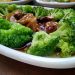 Steamed broccoli in savory sauce with mushrooms on a white plate.