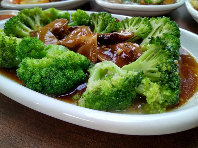 Steamed broccoli in savory sauce with mushrooms on a white plate.