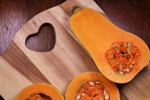 Half butternut squash on a wooden cutting board with heart design.