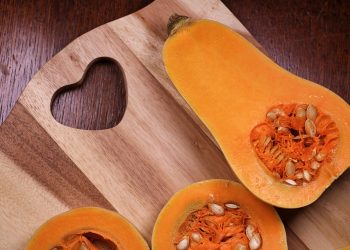 Half butternut squash on a wooden cutting board with heart design.