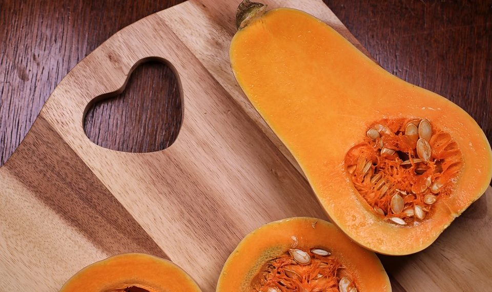 Half butternut squash on a wooden cutting board with heart design.