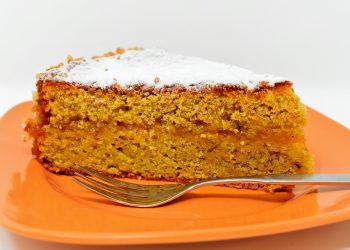 Slice of carrot cake on an orange plate, topped with powdered sugar.