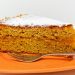 Slice of carrot cake on an orange plate, topped with powdered sugar.