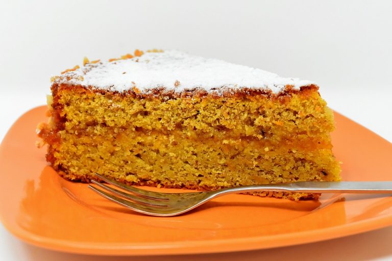 Slice of carrot cake on an orange plate, topped with powdered sugar.