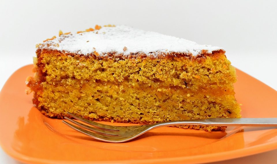 Slice of carrot cake on an orange plate, topped with powdered sugar.