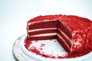Red velvet cake with cream cheese layers on a white plate.