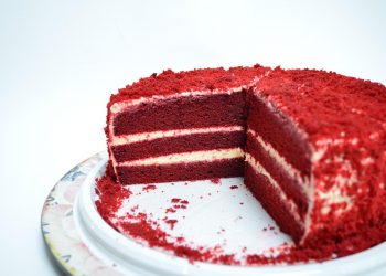 Red velvet cake with cream cheese layers on a white plate.