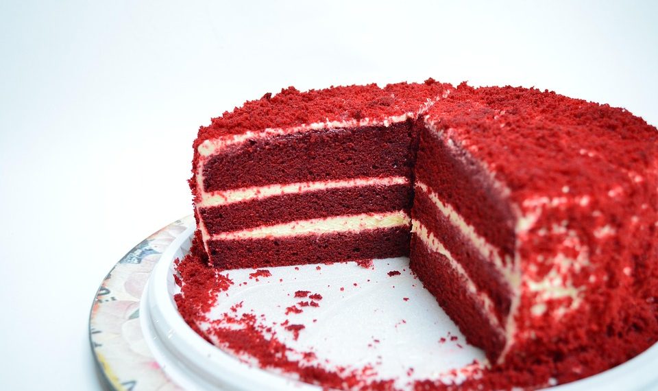 Red velvet cake with cream cheese layers on a white plate.