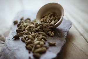Cardamom pods spilling from a bowl on a stone tray.