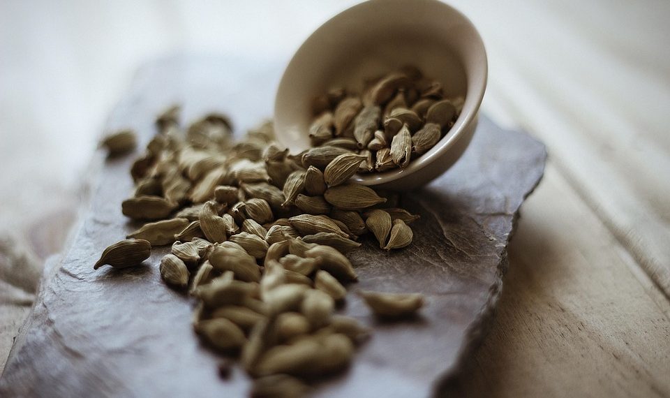 Cardamom pods spilling from a bowl on a stone tray.