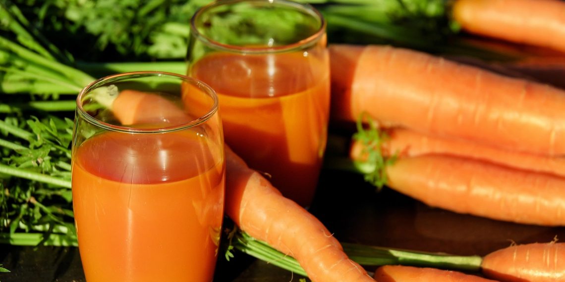 Carrot juice in glasses with fresh carrots on a table.
