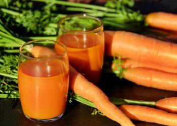 Carrot juice in glasses with fresh carrots on a table.