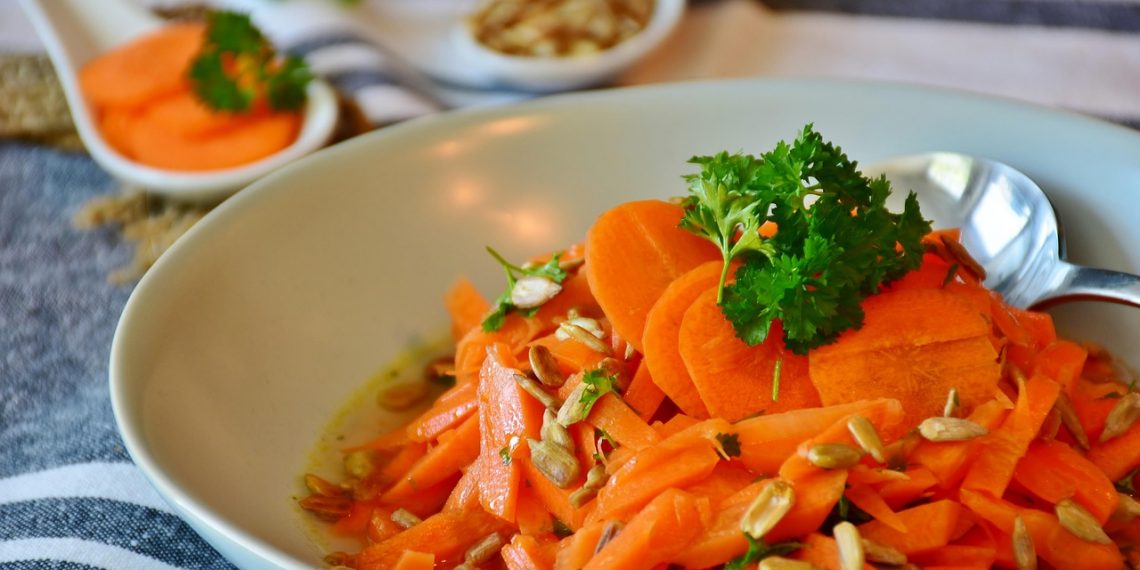 Fresh carrot salad with parsley and seeds on a white plate.