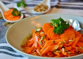 Fresh carrot salad with parsley and seeds on a white plate.