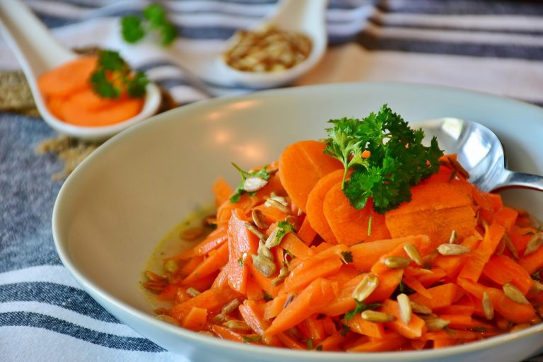 Fresh carrot salad with parsley and seeds on a white plate.