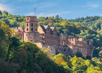 Heidelberg Castle nestled in lush forest, viewed from afar.