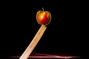 Apple balanced on a sharp-edged plank against a dark backdrop.