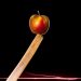 Apple balanced on a sharp-edged plank against a dark backdrop.