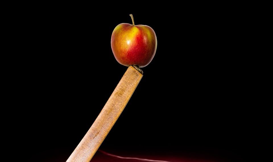 Apple balanced on a sharp-edged plank against a dark backdrop.