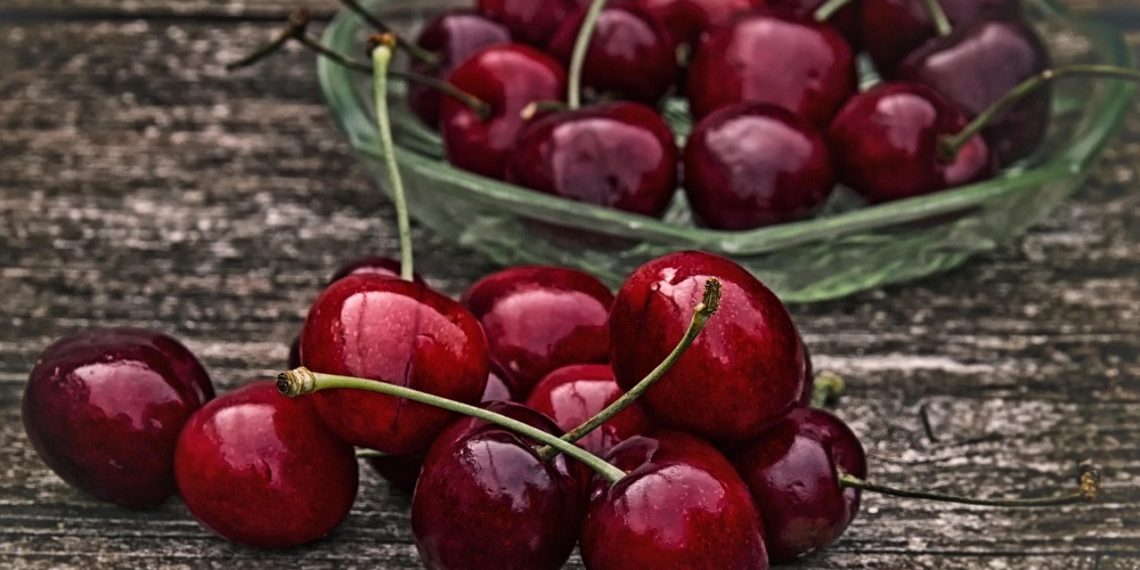 Juicy red cherries in a glass bowl on wooden table.