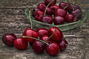 Juicy red cherries in a glass bowl on wooden table.