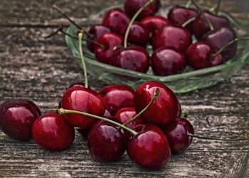 Juicy red cherries in a glass bowl on wooden table.
