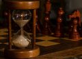 Hourglass on chessboard with chess pieces in focus.