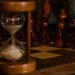 Hourglass on chessboard with chess pieces in focus.