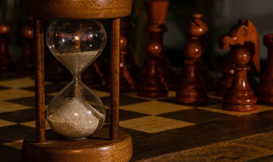 Hourglass on chessboard with chess pieces in focus.