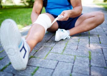 Man wrapping knee with bandage on a park path.