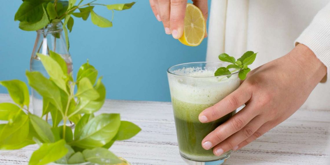 Preparing green smoothie with lemon slice.