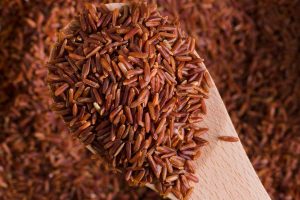 Spoonful of red rice grains spilling over a table.