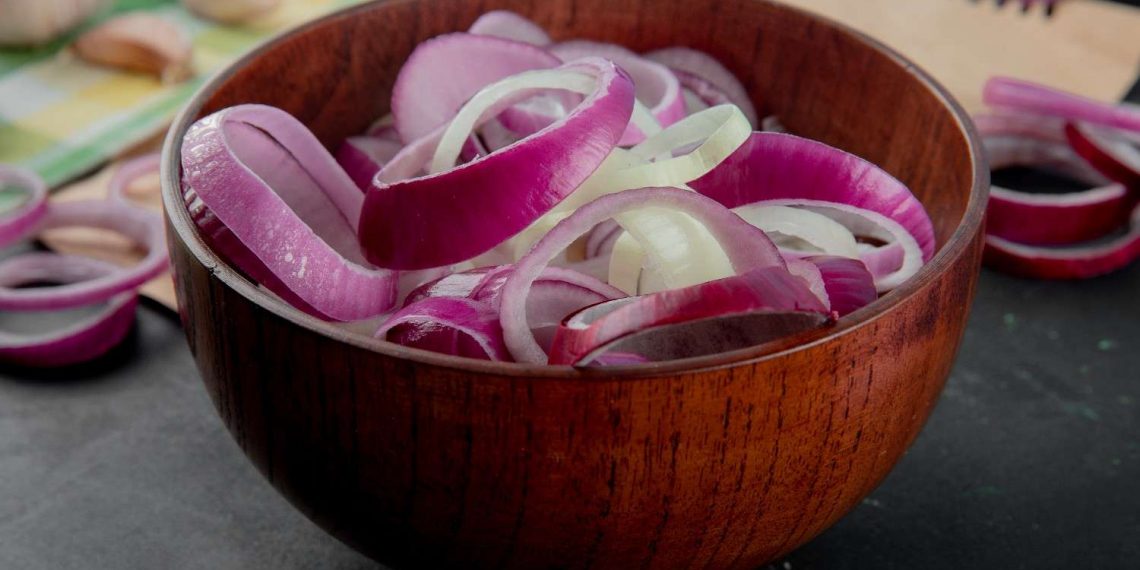 Sliced red onions in a wooden bowl on kitchen counter.