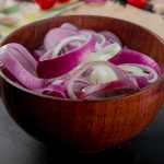 Sliced red onions in a wooden bowl on kitchen counter.