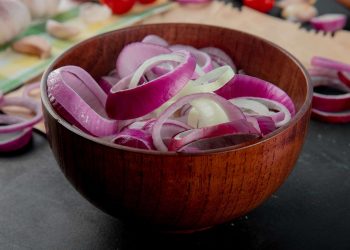 Sliced red onions in a wooden bowl on kitchen counter.
