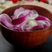 Sliced red onions in a wooden bowl on kitchen counter.