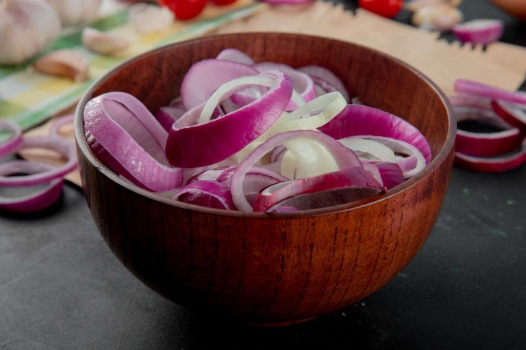 Sliced red onions in a wooden bowl on kitchen counter.