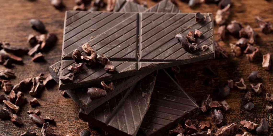 Stacked dark chocolate squares with cocoa nibs scattered.
