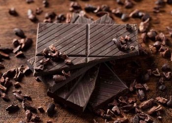 Stacked dark chocolate squares with cocoa nibs scattered.