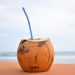 Coconut with a straw on a sandy beach background.