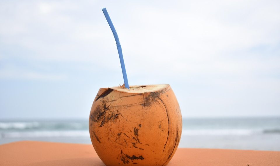 Coconut with a straw on a sandy beach background.
