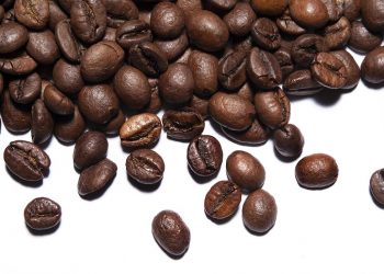 Roasted coffee beans scattered on white background.