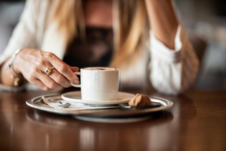 Woman enjoying a cappuccino at a cafe table.